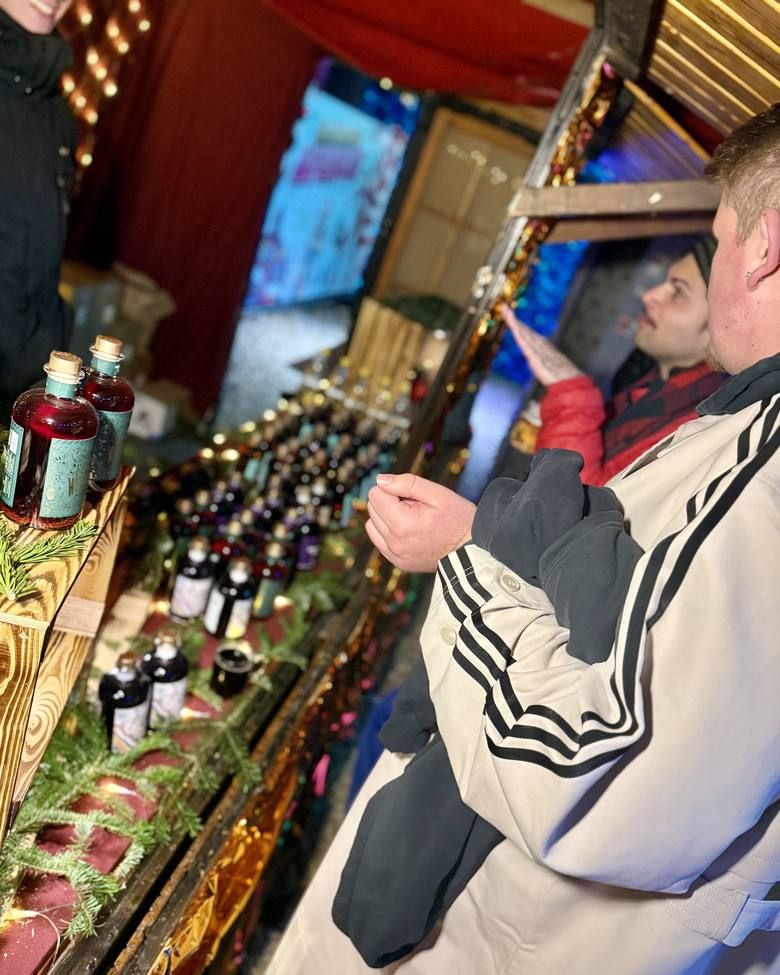 Auf einem Weihnachtsmarkt betrachten zwei Besucher die Auswahl an Glühweinsorten an einem festlich geschmückten Stand.