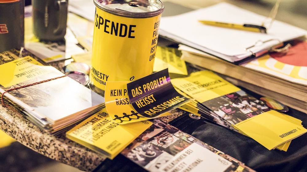 Auf einem Infotisch liegen Flyer, Aufkleber und Broschüren von Amnesty International, daneben steht eine Spendendose.