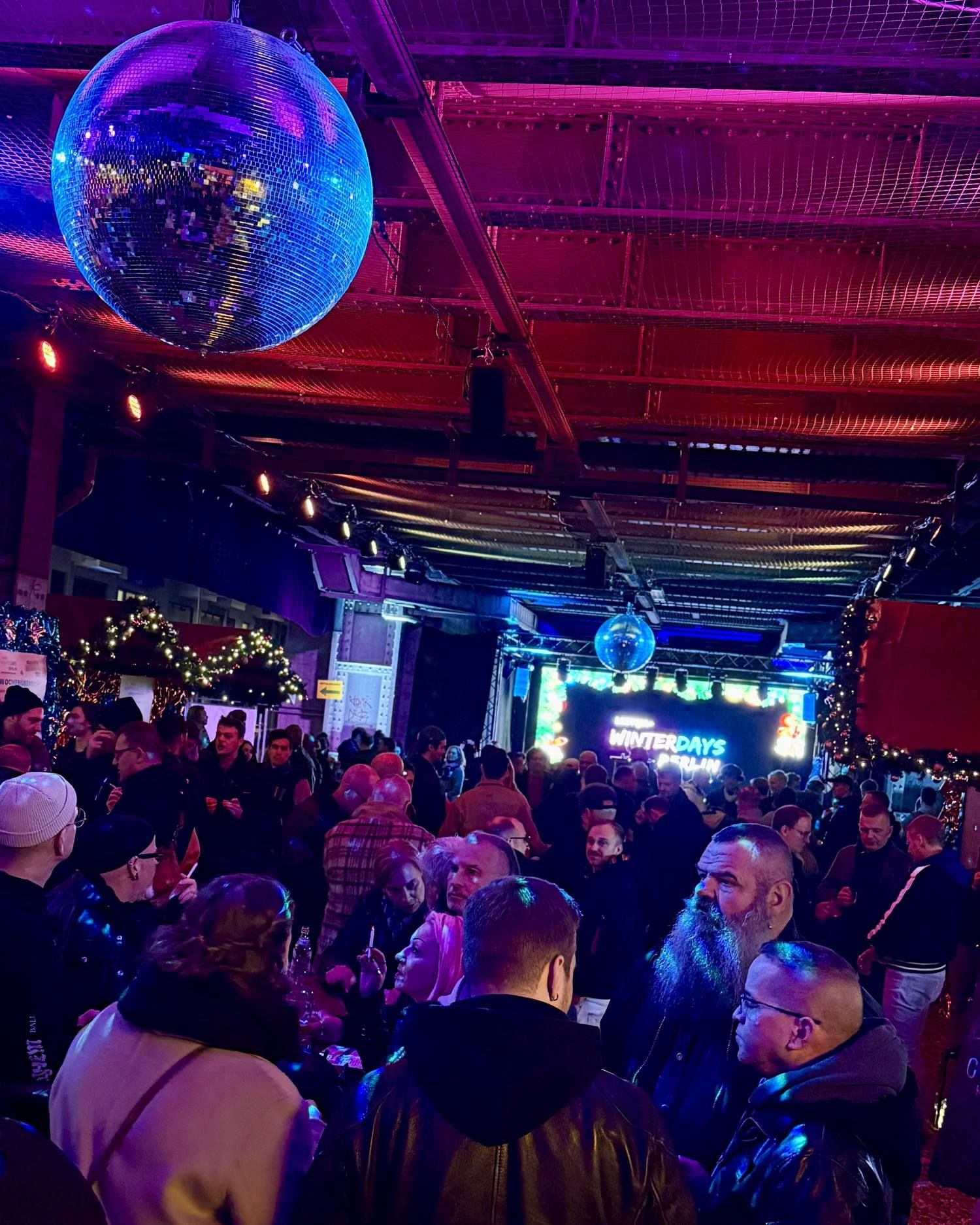Viele Menschen feiern und unterhalten sich ausgelassen bei den Winterdays in Berlin unter einer großen bunten Discokugel.